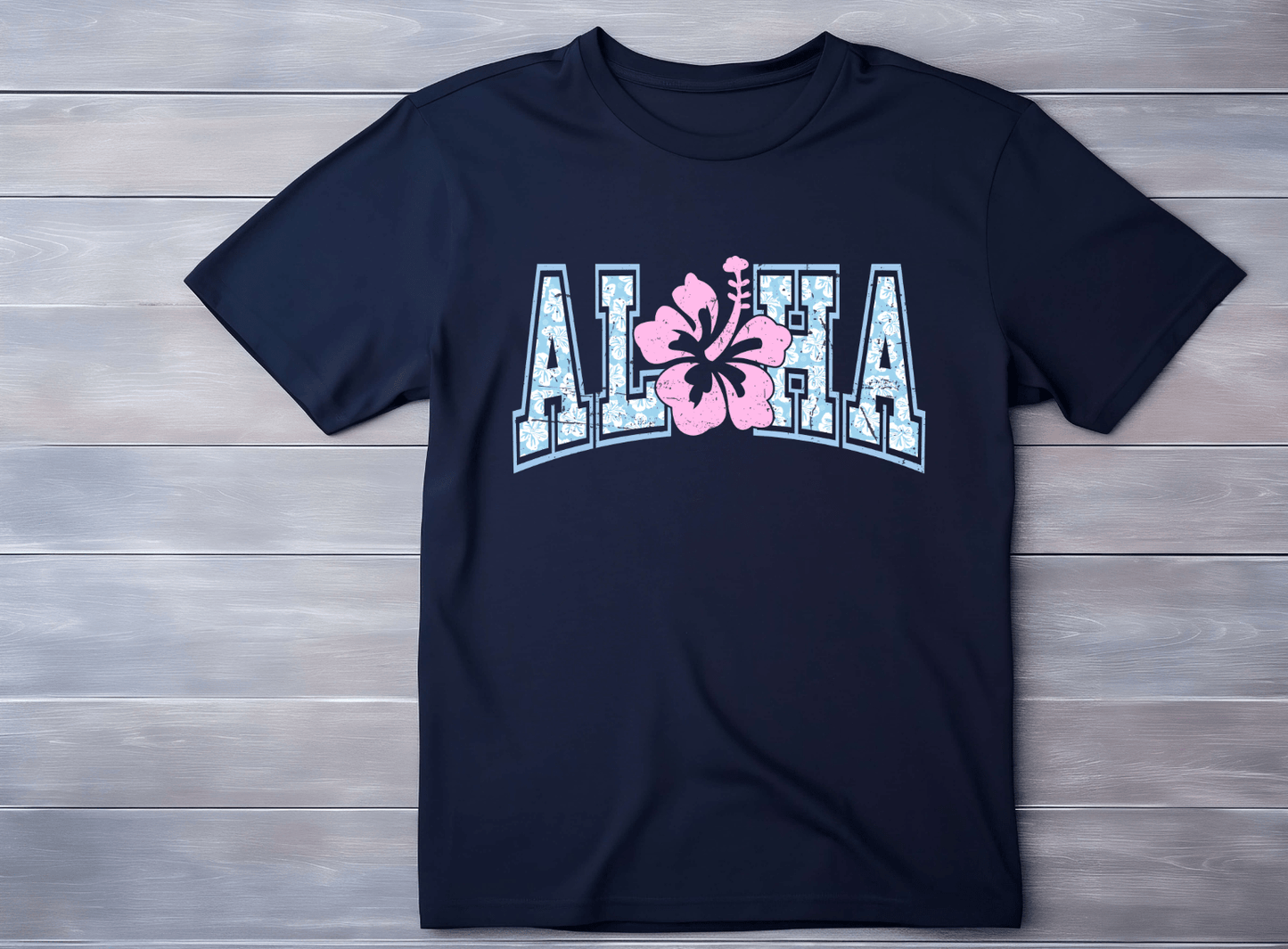 A navy blue Aloha T-shirt by DB Custom Creations, with a bold DTF design: ALOHA in large white letters outlined in blue and a pink hibiscus flower as the O, shown on a light wooden surface.
