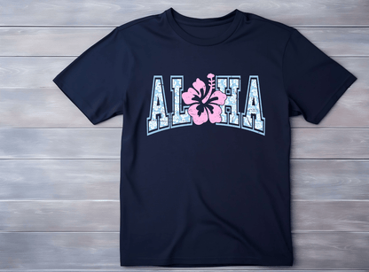 A navy blue Aloha T-shirt by DB Custom Creations, with a bold DTF design: ALOHA in large white letters outlined in blue and a pink hibiscus flower as the O, shown on a light wooden surface.