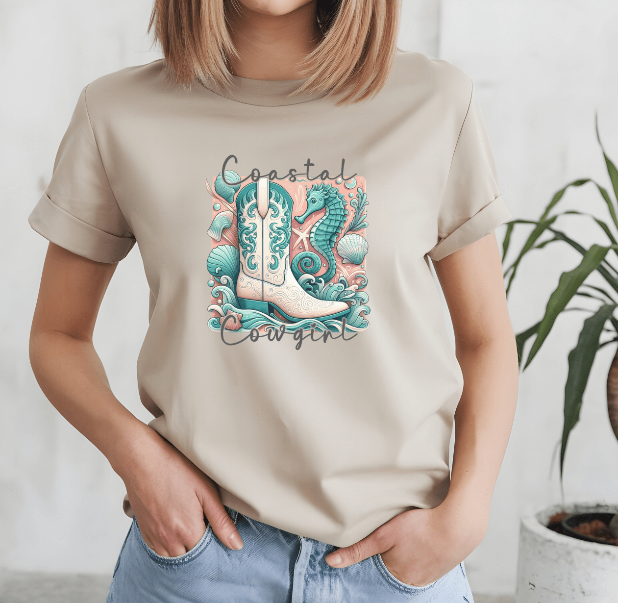 A woman wears a beige Coastal Cowboy t-shirt by DB Custom Creations, featuring an illustrated cowboy boot with seahorses, shells, and seaweed. Coastal Cowgirl is printed above and below the design using high-quality DTF printing.