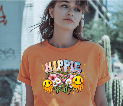 A young woman in hoop earrings wears the orange Hippie t-shirt by DB Custom Creations, featuring Hippie Soul, flowers, and melting smiley faces printed with vibrant DTF, as she stands outside by a cactus and graffiti wall.