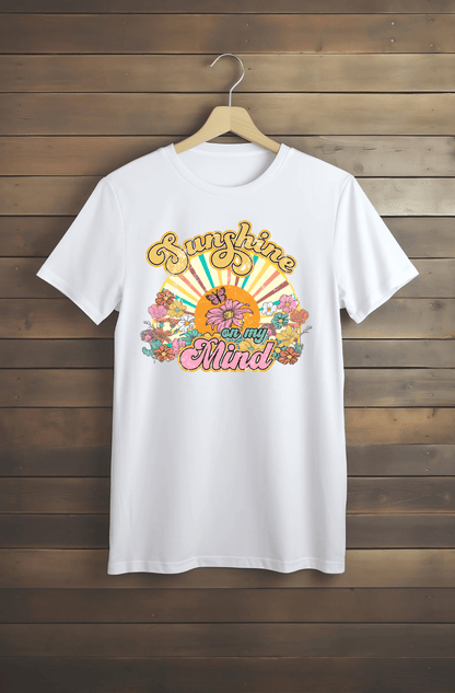 The “Sunshine” white T-shirt by DB Custom Creations features a vibrant 11-inch DTF print with retro flowers, a sun, and the phrase “Sunshine on my Mind” in yellow and pink decorative fonts.