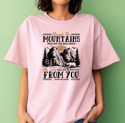 A woman wears the Through the Mountain pink t-shirt by DB Custom Creations, made with DTF printing. It features mountains and trees with the phrase: Though the mountains move, my love will not be removed from you. Isaiah 54:10.