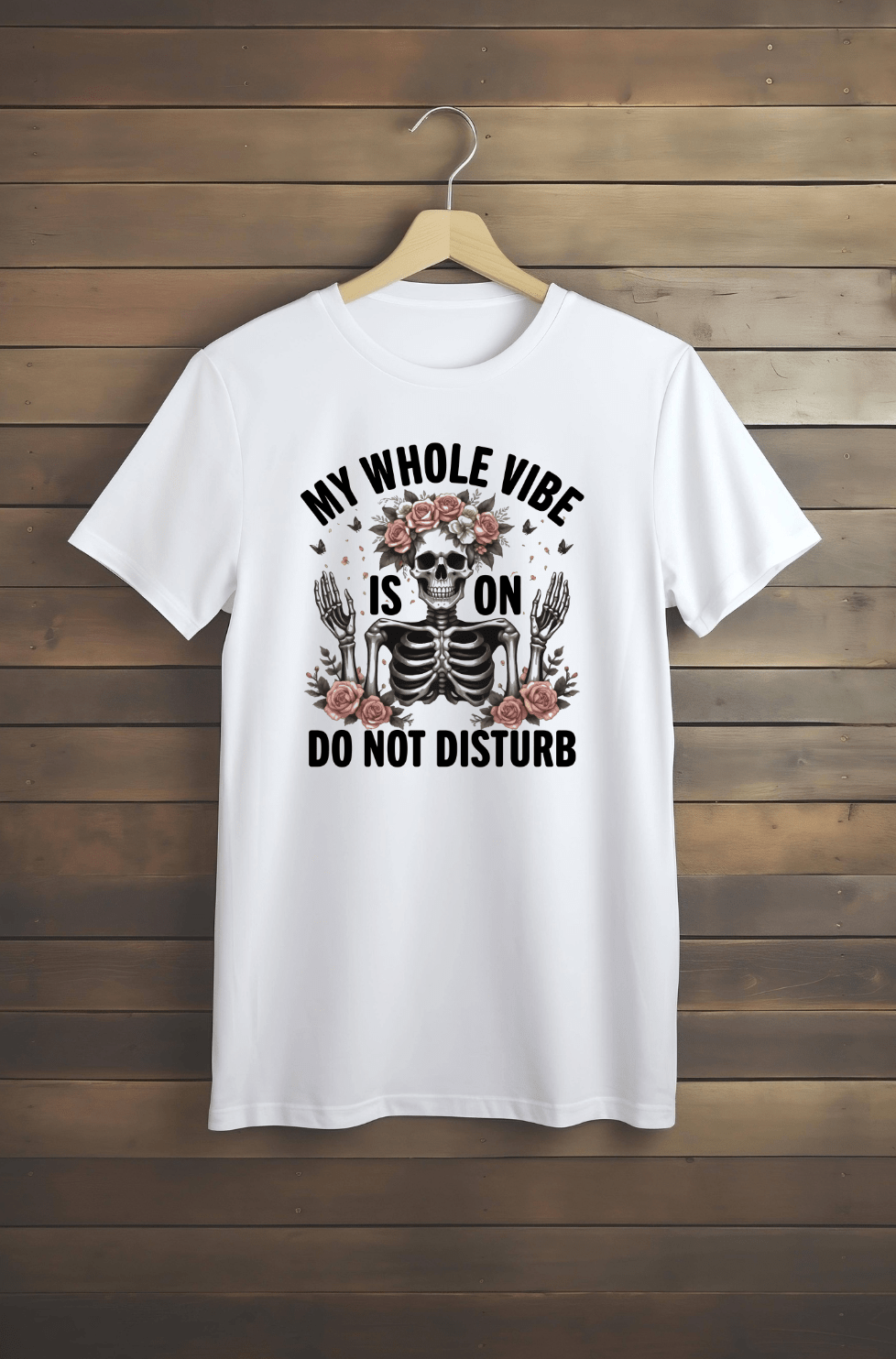 The “Whole Vibe” white t-shirt by DB Custom Creations features a skeleton and flower design with the text “MY WHOLE VIBE IS ON DO NOT DISTURB,” printed in vibrant DTF, displayed on a wooden hanger against a plank wall.